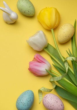 Paskalya yumurtaları ve renkli laleler sarı bir yüzeyi süsleyerek neşeli bir bahar atmosferi yaratıyor.