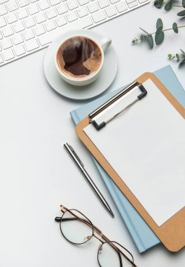 Beyaz arkaplanda klavye, kahve, dosya, bardak ve okaliptüs dalları olan ofis masası