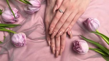 Mor lalelerin yanında nişan yüzüğüyle yeni manikürünü gösteren bir kadın.