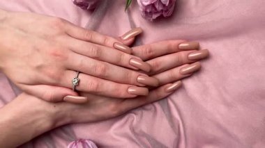 Mor lalelerin yanında nişan yüzüğüyle yeni manikürünü gösteren bir kadın.