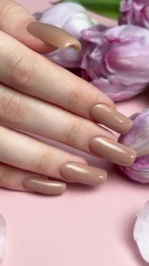 Mor lalelerin yanında nişan yüzüğüyle yeni manikürünü gösteren bir kadın.