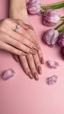 Mor lalelerin yanında nişan yüzüğüyle yeni manikürünü gösteren bir kadın.