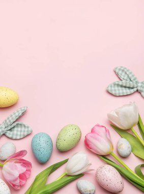 Paskalya yumurtaları ve laleler pembe arka planda fotokopi alanı olan bir çerçeve oluşturuyor.