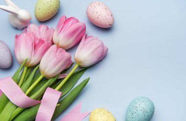 Paskalya yumurtaları ve pembe laleler pembe kurdeleyle bağlanmış pastel mavi arka planda bir bahar tatili sınırı oluşturuyorlar.