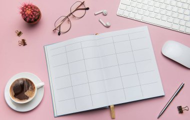 Açık defter, kahve, kaktüs, gözlük, kulaklık, kalem, klavye ve fareli ev ofisi çalışma alanı pembe arka planda yatıyor