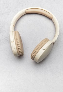 Gri taştan bir yüzeyde dinlenen kablosuz kulaklıklar dinleyicileri yüksek kaliteli seslere davet ediyor.