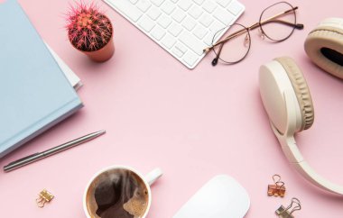 Kahveli, kulaklıklı, klavyeli, fareli, gözlüklü, defterli, kalemli, kaktüslü ve klasörlü pembe bir masa.
