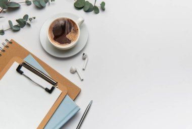 Kahve, okaliptüs, pano, defter, kalem ve kablosuz kulaklıklı ofis masası çalışma alanı verimli bir günü davet ediyor.