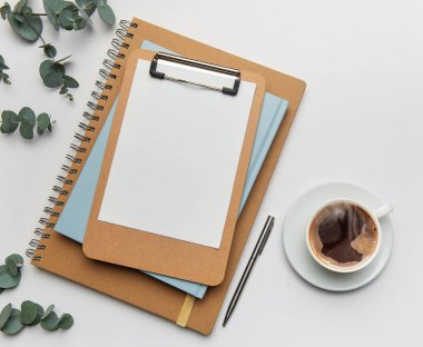 Ofis masası çalışma alanı, pano, boş kağıt, defterler, bir fincan kahve ve okaliptüs filizi, üst görünüm.