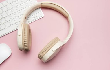 Modern kablosuz kulaklıklar, pembe arka planda klavye ve bilgisayar faresi, şık ve üretken bir çalışma alanı yaratıyor
