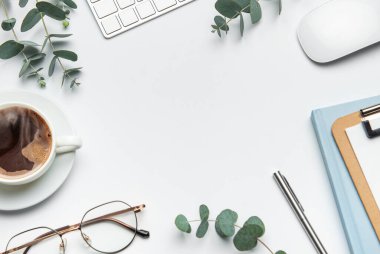 Ökaliptüs dalları, kahve fincanı, klavye, fare, gözlük, kalem ve defterin beyaz masa arkasını çerçevelemesi, iş ve yaşam tarzı blogları için ideal