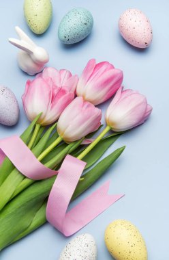 Paskalya yumurtaları ve pembe laleler pembe kurdeleyle bağlanmış pastel mavi arka planda bir bahar tatili sınırı oluşturuyorlar.