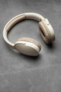 Modern kablosuz kulaklıklar gri bir yüzeyde, müzik dinlemeyi, podcast zevkini veya ses iletişimini temsil ediyor.