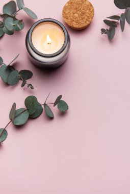 Okaliptüs dalları ve pembe arka planda yanan aromatik mum rahatlatıcı bir atmosfer yaratır.