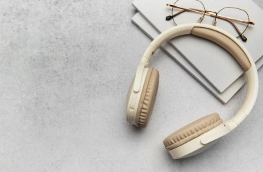 Gri desenli bir yüzeye yerleştirilmiş bej kablosuz kulaklıklar, kitaplar ve gözlükler rahat ve üretken bir atmosfer yaratıyor.