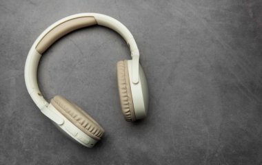 Modern kablosuz kulaklıklar gri bir yüzeyde, müzik dinlemeyi, podcast zevkini veya ses iletişimini temsil ediyor.