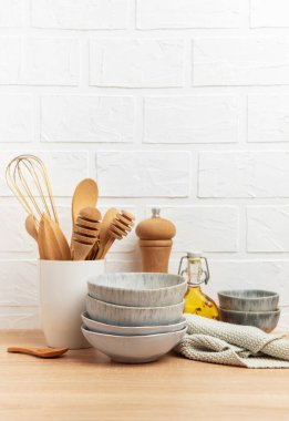 Tahta kaşıklar, çırpı, kase, biber değirmeni, yağ ve katlanmış bulaşık bezi rahat bir mutfak sahnesi oluşturur.