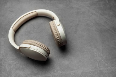 Modern kablosuz kulaklıklar gri bir yüzeyde, müzik dinlemeyi, podcast zevkini veya ses iletişimini temsil ediyor.