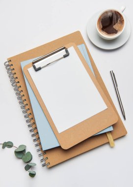 Ofis çalışma alanı beyaz zemin üzerinde pano, kahve, kalem ve defter ile düzenlenmiştir.