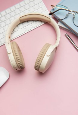 Modern çalışma alanı kablosuz kulaklıklar, klavye, bilgisayar faresi, gözlük, kalem ve pembe arka plan üzerine not defterleri