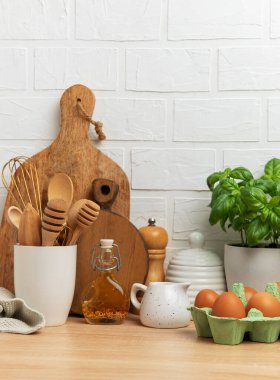 Ahşap kaplar, taze yumurtalar, fesleğen bitkisi ve çeşitli yemek malzemelerinin yer aldığı Rustik mutfak sahnesi samimi ve davetkar bir atmosfer yaratıyor.