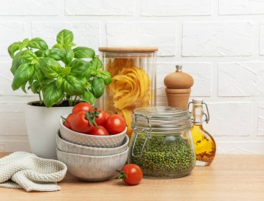 Vişneli domates, fesleğen, makarna, fasulye ve zeytinyağı, sağlıklı bir İtalyan yemeği hazırlamak için ahşap mutfak tezgahında düzenlenir.