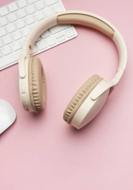 Modern kablosuz kulaklıklar, pembe arka planda klavye ve bilgisayar faresi, şık ve üretken bir çalışma alanı yaratıyor