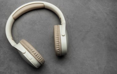 Modern kablosuz kulaklıklar gri bir yüzeyde, müzik dinlemeyi, podcast zevkini veya ses iletişimini temsil ediyor.