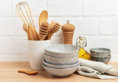 Tahta kaşıklar, çırpı, kase, biber değirmeni, yağ ve katlanmış bulaşık bezi rahat bir mutfak sahnesi oluşturur.