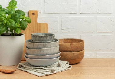 Seramik ve ahşap kaseler mutfak masasına istiflenmiş fesleğen bitkisi, tahta tahta kaşık ve ahşap bir mutfak sahnesi yaratıyor.