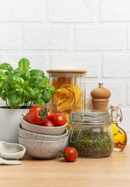 Vişneli domates, fesleğen, makarna, fasulye ve zeytinyağı, sağlıklı bir İtalyan yemeği hazırlamak için ahşap mutfak tezgahında düzenlenir.