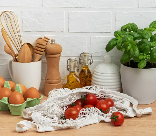 Taze vişneli domatesler, fesleğen, yumurta ve zeytinyağı şişeleri sağlıklı bir pişirme sahnesi oluşturur.