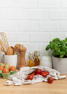 Taze vişneli domatesler, fesleğen, yumurta ve zeytinyağı şişeleri sağlıklı bir pişirme sahnesi oluşturur.