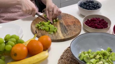 Parlak bir mutfakta sağlıklı meyve salatası hazırlayan genç bir kadın.