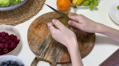 Mutfak masasında taze malzemelerle çevrili kivi meyvesi soyan genç bir kadın.