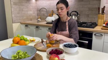 Genç kadın sağlıklı bir yemek hazırlıyor, portakalı tahta üzerinde dilimliyor.