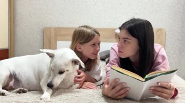 İki kız kardeş ve köpekleri yatakta kitap okuyarak güzel vakit geçiriyorlar.