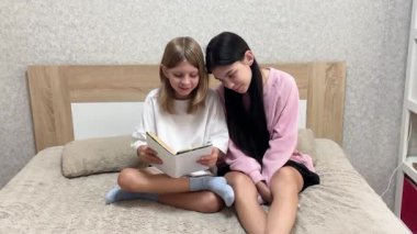 İki kız kardeş birlikte sakin bir anın tadını çıkarıyorlar, yatakta kitap okuyorlar.