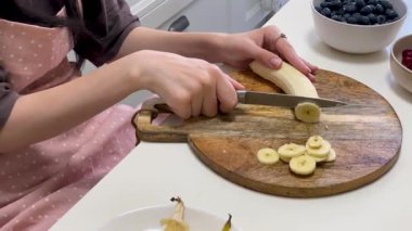 Şef canlı meyve salatası için muz dilimliyor. Çeşit çeşit böğürtlen ve narenciye ile modern mutfak ortamında.