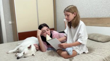 İki kız kardeş ve köpekleri yatakta kitap okuyarak güzel vakit geçiriyorlar.