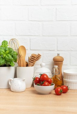 Mutfak tezgahında mutfak malzemeleri, taze domatesler, fesleğen ve zeytinyağı beyaz tuğla duvara karşı modern bir mutfak sahnesi hazırlıyor.