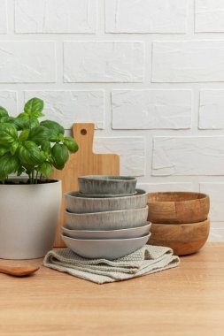 Seramik ve ahşap kaseler mutfak masasına istiflenmiş fesleğen bitkisi, tahta tahta kaşık ve ahşap bir mutfak sahnesi yaratıyor.