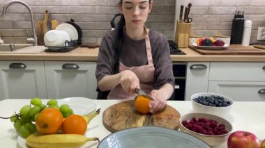 Bir portakalı ahşap bir tahtanın üzerinde dikkatlice kes, çeşitli meyvelerle çevrili.