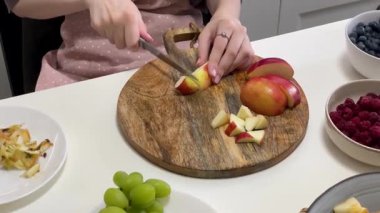 Profesyonel bir aşçı, ahşap kesim tahtasıyla elma dilimliyor, modern bir mutfakta taze meyve salatası hazırlıyor.