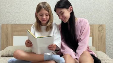 İki kız kardeş birlikte sakin bir anın tadını çıkarıyorlar, yatakta kitap okuyorlar.