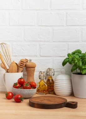 Ahşap kesim tahtası, kiraz domatesleri, baharatlar ve fesleğen bitkisi rahat bir mutfak ortamı yaratıyor.