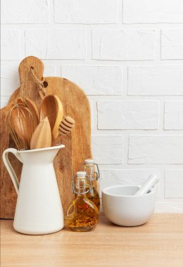 Ahşap mutfak aletleri, kesme tahtaları, yağ şişeleri ve ahşap bir tezgahta beyaz tuğladan bir duvara karşı dizilmiş bir havan ve tokmak, kırsal bir mutfak sahnesi yaratıyor.