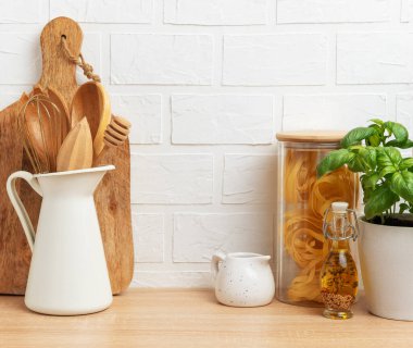 Mutfak tezgahında ahşap kaplar, makarna, fesleğen, yağ ve beyaz tuğla duvar zeminine karşı kopyalama alanı