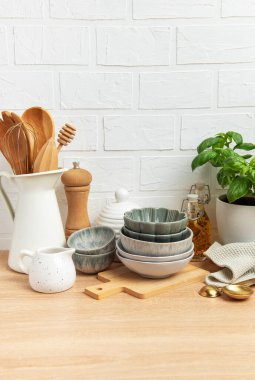 Tabaklar, tahta kaşıklar ve fesleğen bitkisi de dahil olmak üzere çeşitli mutfak malzemeleri beyaz tuğlalı bir duvara karşı ahşap bir tezgahta güzelce düzenlenmiştir.