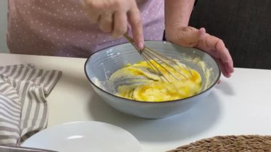 Şef bir kasede yumurta, şeker ve tereyağı çırpıyor, kek hamuru hazırlıyor.